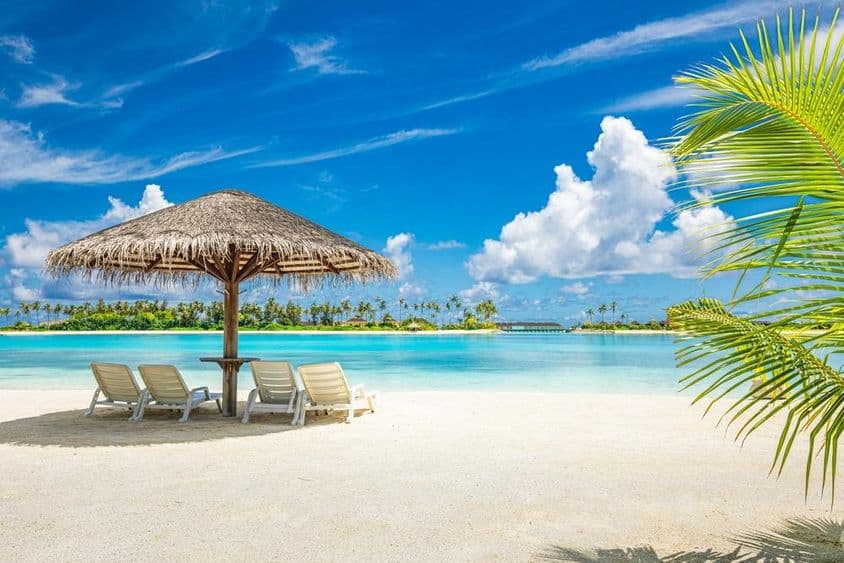 Praia de areia das Maldivas com guarda-sol e espreguiçadeira.