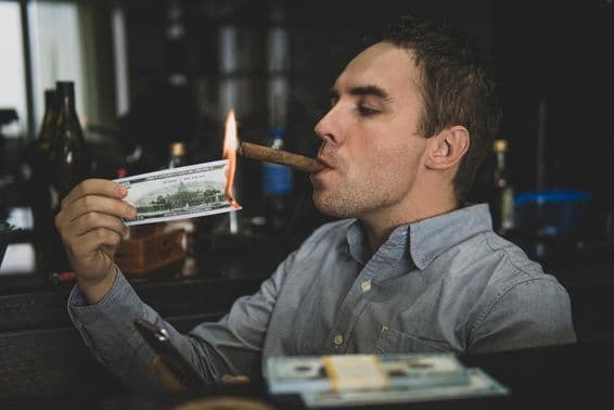 Jovem homem bonito acendendo charuto com cédula de cem dólares em um bar.