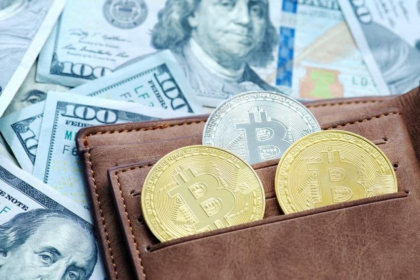 Bitcoin dourado com uma carteira, abaixo notas de dólar.