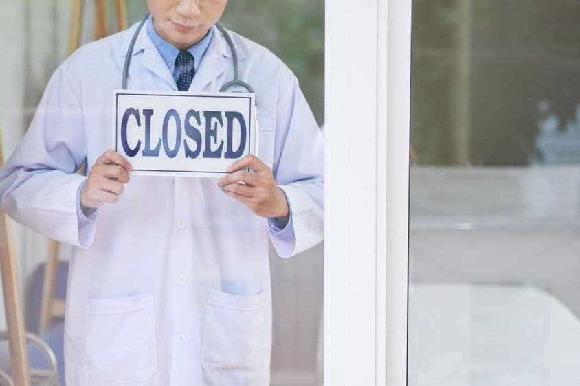 Um homem em uniforme médico segurando uma placa de fechado.