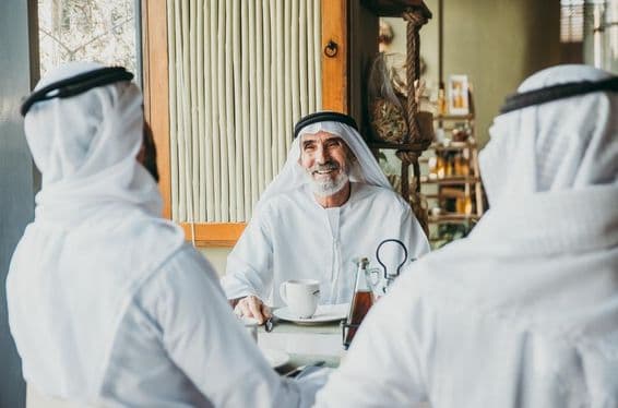 Três empresários apreciando chá em Dubai enquanto vestem trajes tradicionais dos Emirados.