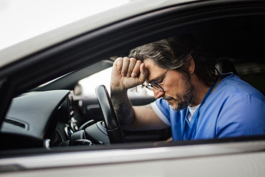 Médico no carro, exausto.