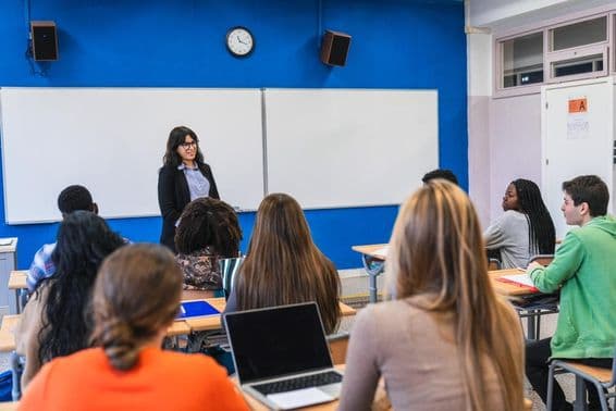 Estudantes do ensino médio ouvindo seu professor ministrar uma aula em uma sala de aula moderna.