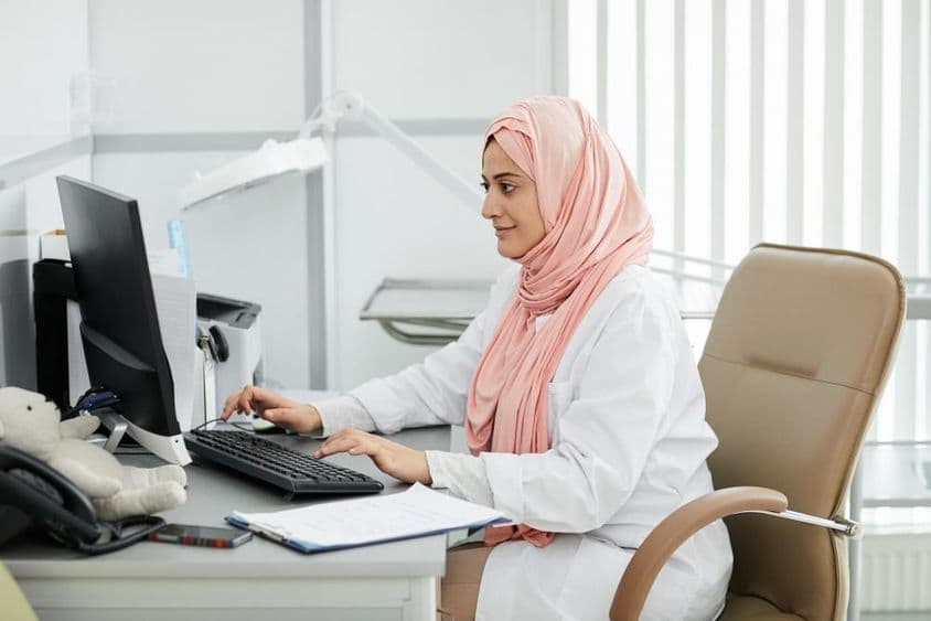 Uma jovem mulher do Oriente Médio usando um hijab trabalhando como enfermeira em uma clínica médica.