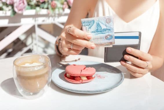 Menina pagando o café da manhã em um café em Dubai com dirhams.