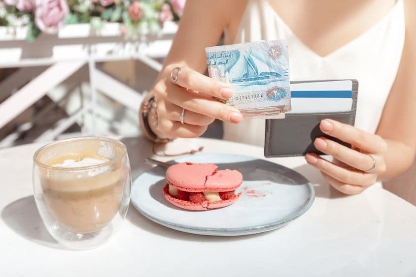 Menina pagando o café da manhã em um café em Dubai com dirhams.