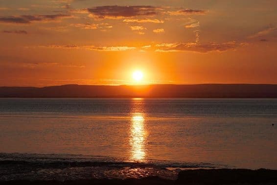 Pôr do sol refletindo na água e nas nuvens durante o solstício de verão.