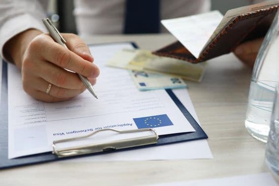 Um homem segurando um passaporte e preenchendo informações pessoais em um pedido de visto Schengen.