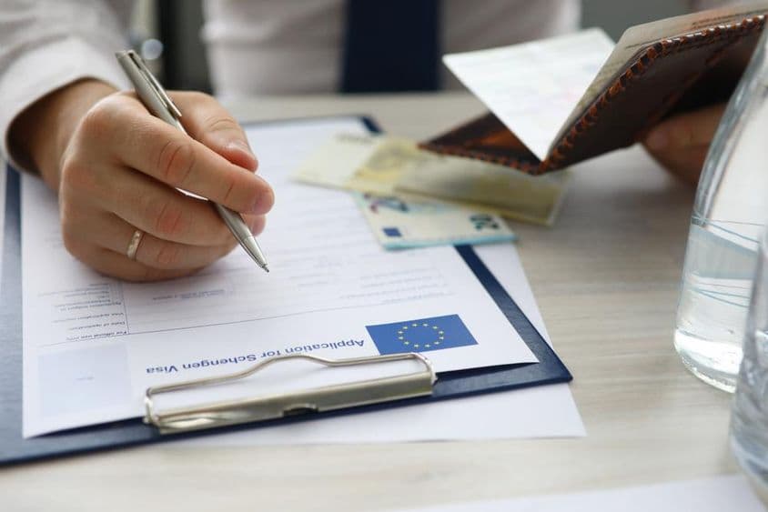 Um homem segurando um passaporte e preenchendo informações pessoais em um pedido de visto Schengen.