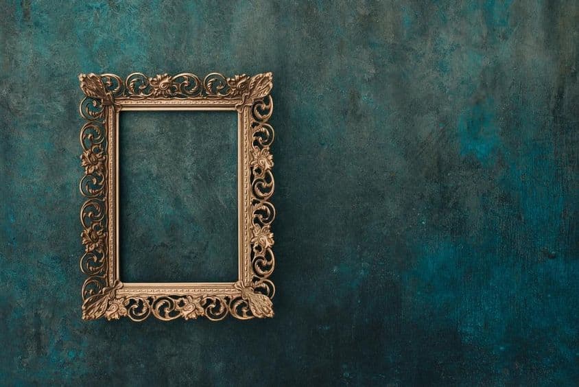 Moldura metálica vintage em bronze com rendilhado em uma parede envelhecida azul e verde.