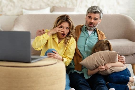 Pais de meia-idade e filha chocados assistindo filme online em laptop.