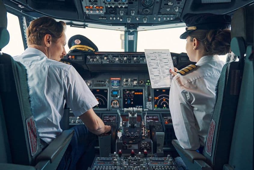 Um capitão e uma copiloto sentados na cabine de avião.