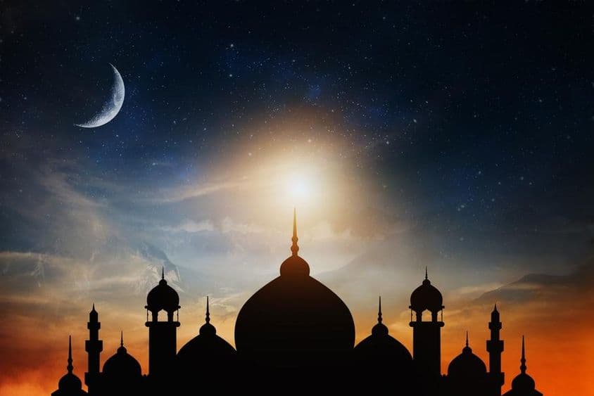 Cúpulas de mesquita contra um céu crepuscular azul profundo com uma lua crescente ao fundo.