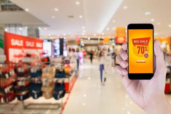 Smartphone exibindo tela de aplicativo de grande promoção com fundo borrado de shopping.