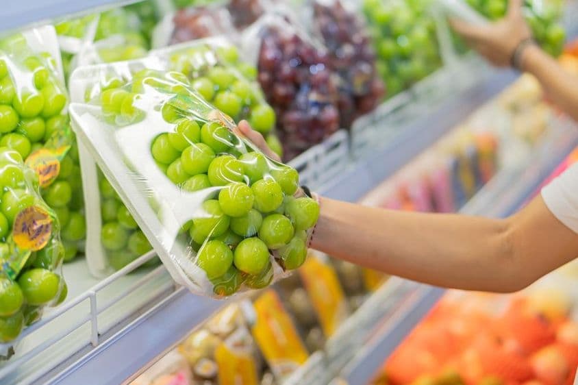 Prateleiras cheias de várias frutas, incluindo uvas vermelhas e outros produtos embalados.