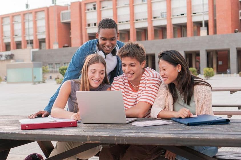 Um grupo de estudantes usando um laptop enquanto pesquisa informações para um projeto ao ar livre.