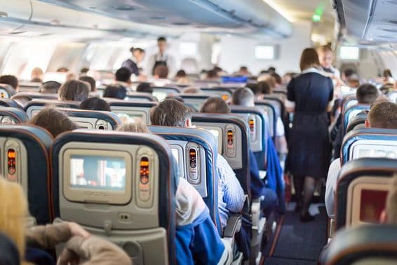 Interior de um avião com pessoas, assentos e comissários de bordo.