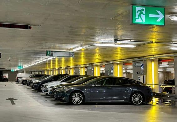 Luzes neon amarelas iluminam espaços reservados para veículos elétricos.
