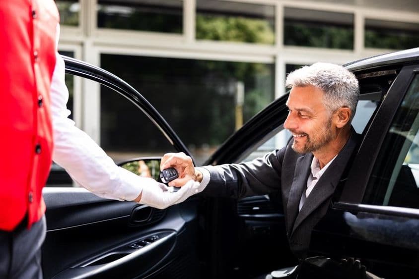 Empresário entrega chaves do carro para manobrista no estacionamento de hotel.