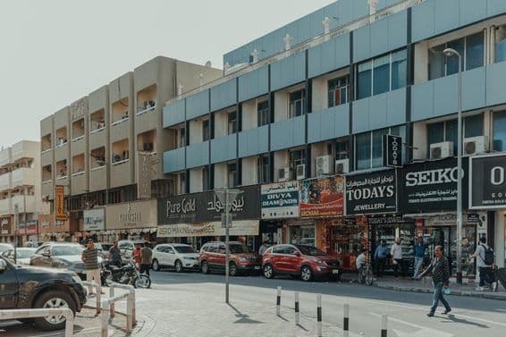 Rua movimentada em Bur Dubai com lojas de joias, pedestres e carros em um dia ensolarado.