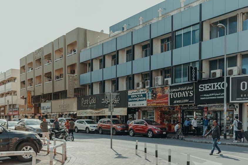 Rua movimentada em Bur Dubai com lojas de joias, pedestres e carros em um dia ensolarado.