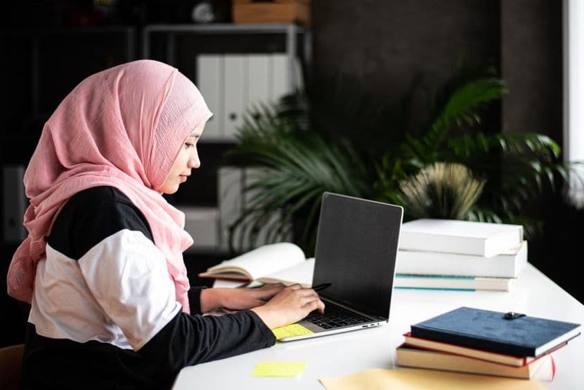 Uma bela mulher muçulmana estuda em casa usando um laptop.