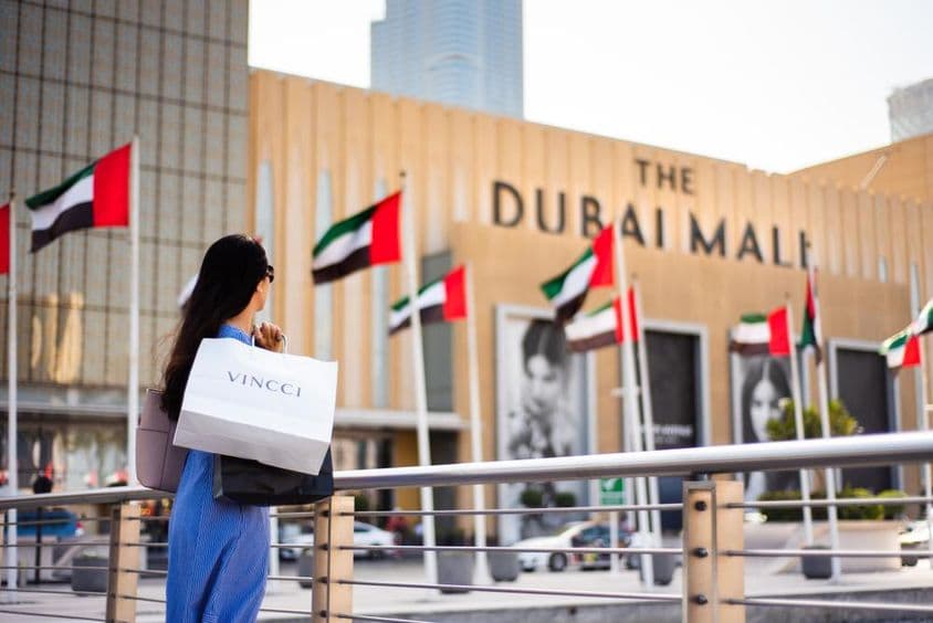 Turista asiático com sacolas de compras na entrada principal do Dubai Mall.