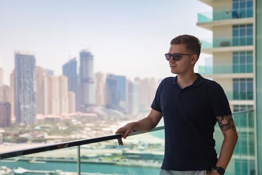 Um jovem de óculos de sol em uma varanda de arranha-céu com vista para Dubai.