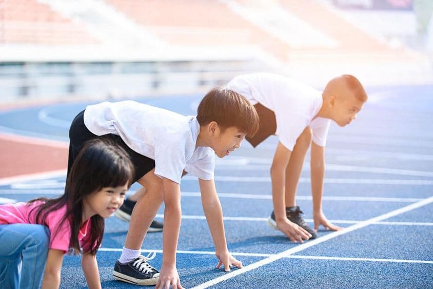 Crianças se preparando para uma corrida em uma pista azul.