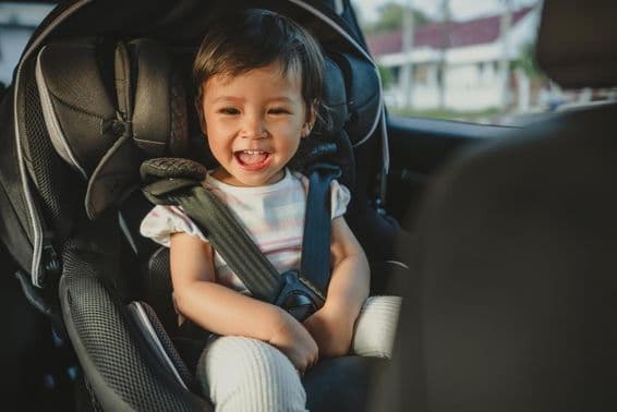 Criança feliz sentada em uma cadeirinha de carro.