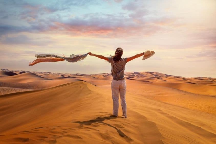 Uma turista mulher está no Deserto Vermelho, em Dubai, acenando seu lenço ao vento quente.