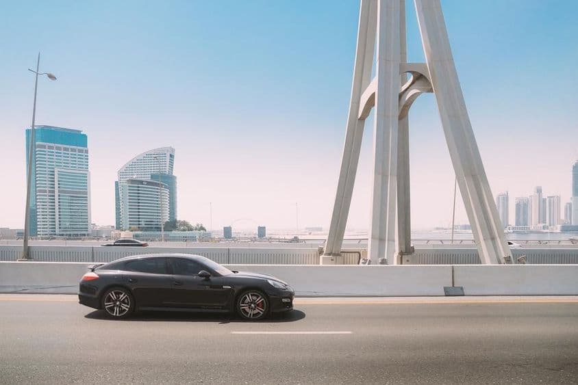Carro Porsche Panamera preto se movendo em uma rua da cidade de Dubai.