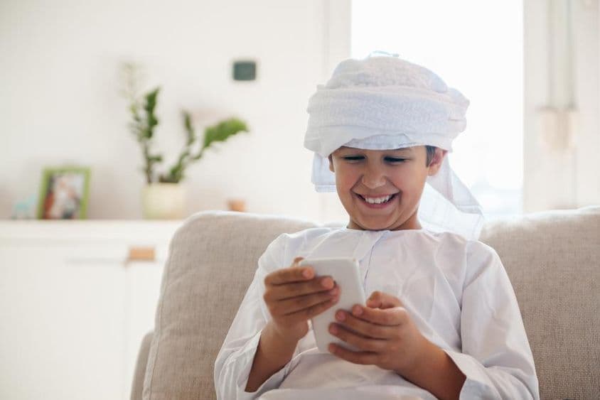 Menino árabe usando um smartphone em casa.