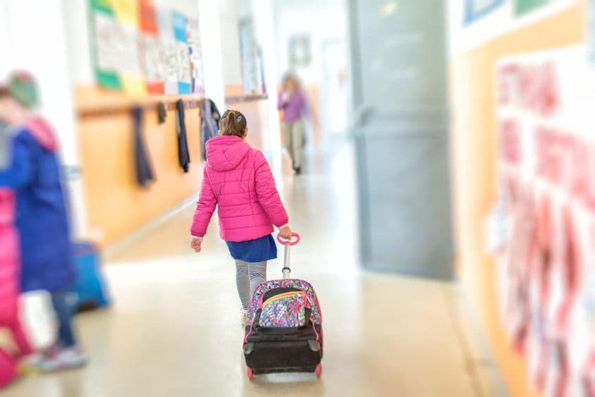 Uma jovem menina puxa uma mochila escolar de rodinhas.