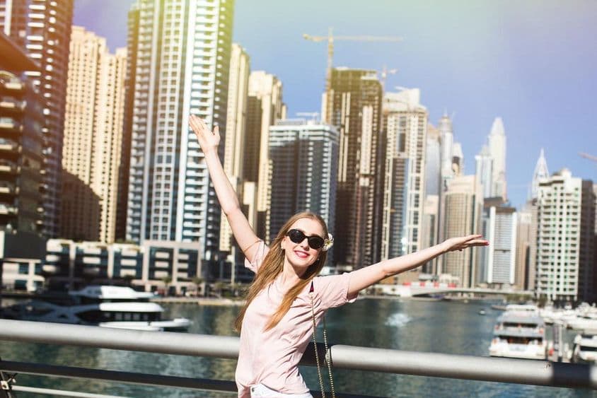 Sol ilumina uma mulher estilosa levantando a mão em uma ponte em algum lugar de Dubai.