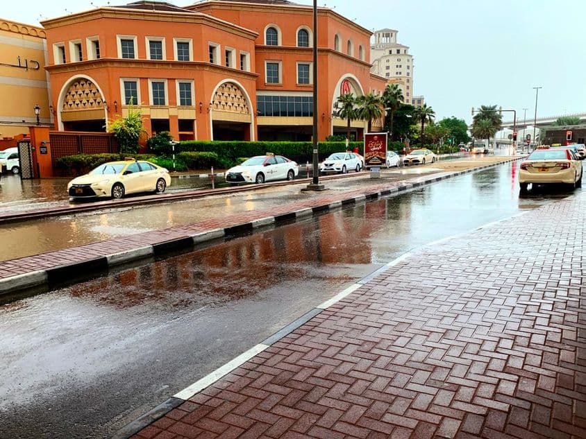 Carros dirigindo por ruas alagadas de Dubai na chuva.