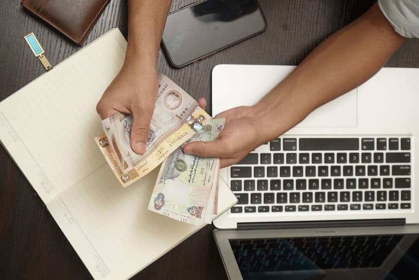 Um homem contando um maço de notas de dirham dos Emirados Árabes Unidos.