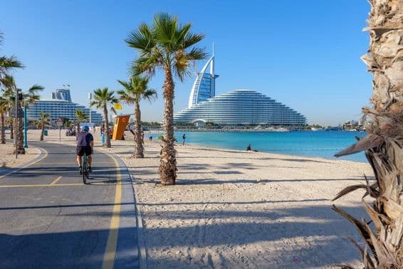 Vista do Burj Al Arab ao longo de uma ciclovia ladeada por palmeiras na Kite Beach Dubai.