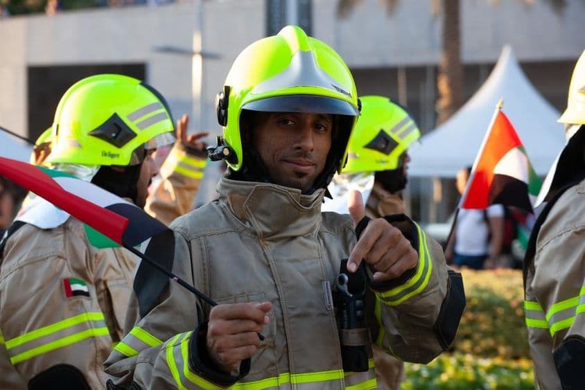 Bombeiros dos Emirados Árabes Unidos caminhando com a bandeira dos Emirados na ocasião do feriado nacional.