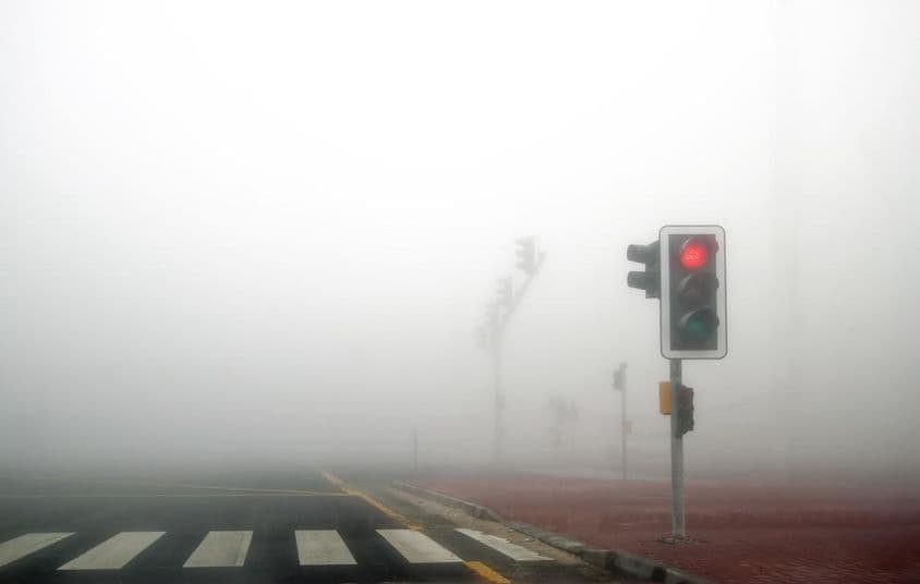 Névoa em uma estrada de Dubai, sinal vermelho piscando.