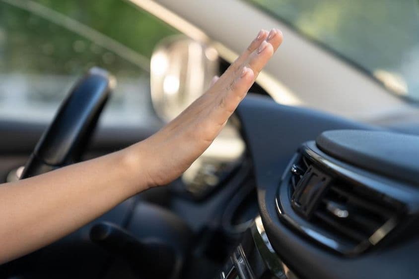 A mão de uma mulher verifica o painel do ar-condicionado em um carro.
