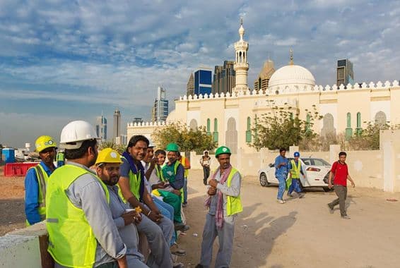 Trabalhadores da construção civil descansando ao lado de uma mesquita no moderno centro de Dubai.