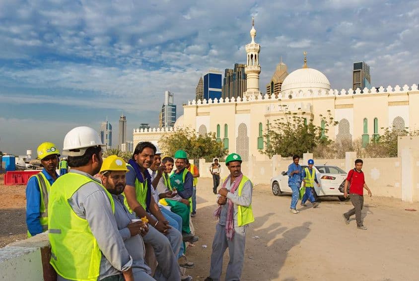 Trabalhadores da construção civil descansando ao lado de uma mesquita no moderno centro de Dubai.