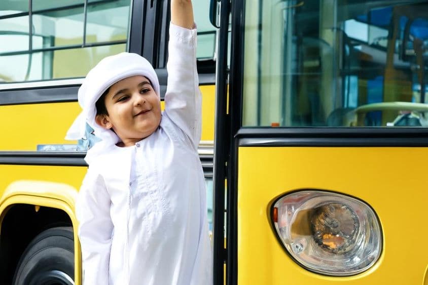 Estudante de escola primária árabe perto de um ônibus escolar amarelo.