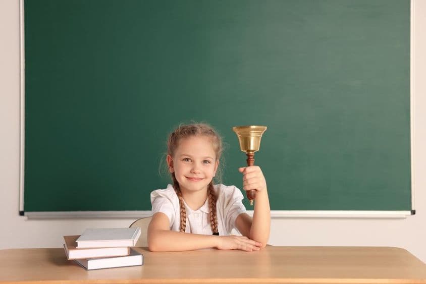 Aluno sentado à mesa com sino escolar em uma sala de aula.