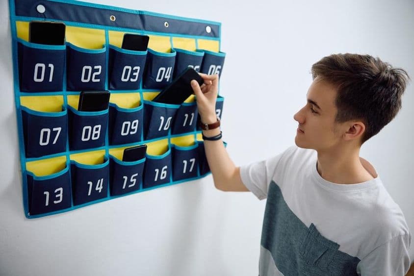 Estudante deixa smartphone em organizador de parede.