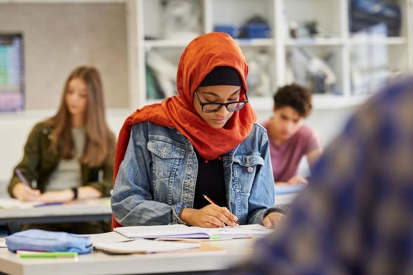 Jovem estudante feminina estudando de hijab enquanto toma notas.