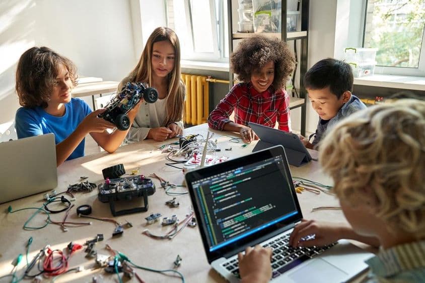 Crianças escolares construindo carros robóticos usando computadores e programação.