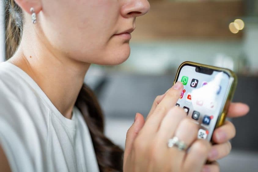 Mulher segurando um iPhone com aplicativo de chat do WhatsApp na tela.