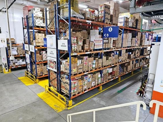 Depósito com sistemas de prateleiras, categorias de produtos rotuladas e sinalizações de segurança auxiliando operações tranquilas.
